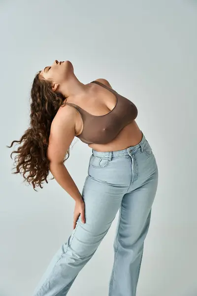 Alluring plus size woman in brown bra and blue jeans with curly hair putting head to behind — Stock Photo