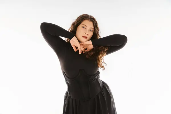 Seductora chica joven de tamaño grande en traje elegante negro con el pelo rizado posando con las manos en gris — Stock Photo