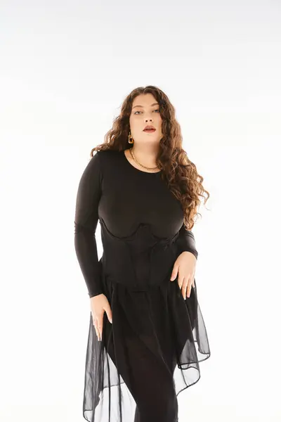 Соблазнительная пышная женщина в черном стильном наряде с вьющимися волосами, позирующая руками на бедрах — стоковое фото
