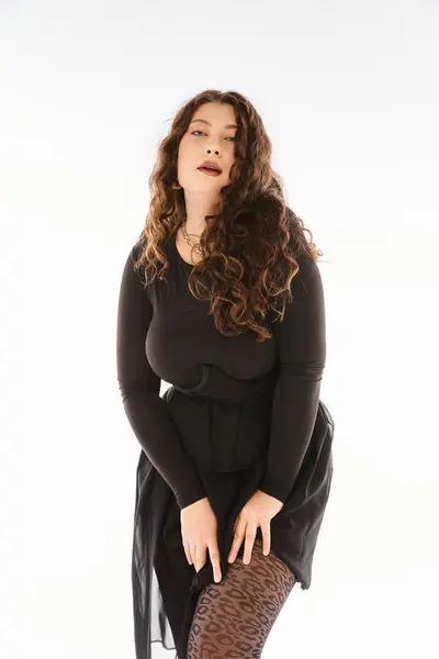 Привлекательная кривая женщина в черном стильном наряде с вьющимися волосами, позирующая руками на бедре — стоковое фото