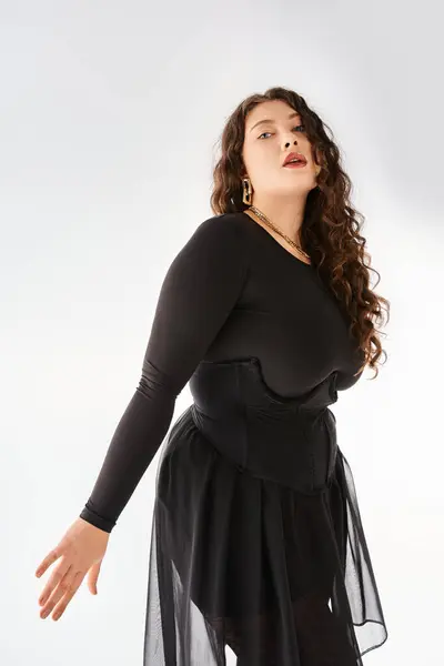 Привлекательный плюс размер женщина в черном стильный наряд с вьющимися волосами позирует на светлом фоне — стоковое фото