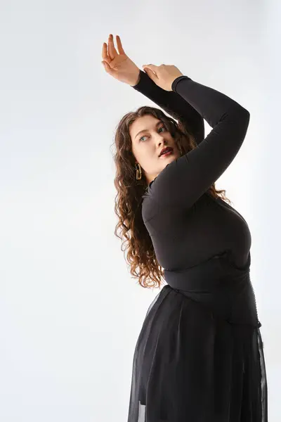 Mujer con curvas en traje elegante negro con el pelo rizado posando de lado y poniendo las manos para arriba - foto de stock