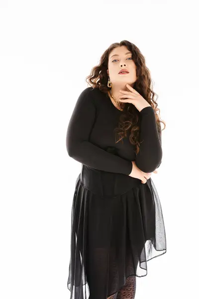 Гламурная плюс размер молодая женщина в черном стильном наряде с вьющимися волосами и рука на шее позирует — стоковое фото