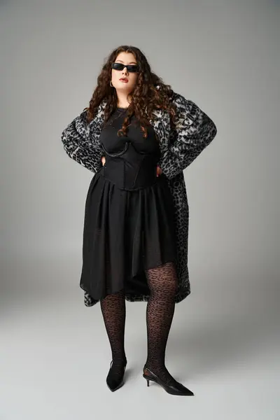 Glamourous plus size jovem mulher em casaco de pele de leopardo e óculos de sol de pé com as mãos na cintura — Fotografia de Stock