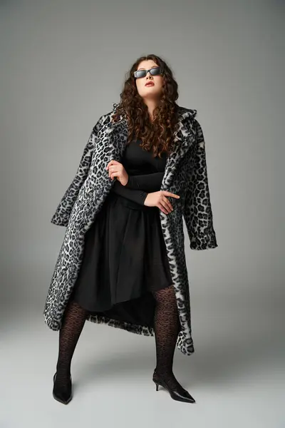 Verführerische Plus-Size-Frau in Sonnenbrille, die sich mit Leopardenfell-Mantel und weit auseinander stehenden Beinen nach vorne lehnt — Stockfoto