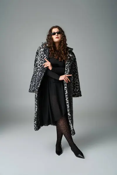 Atraente jovem curvilínea em óculos de sol de pé com casaco de pele de leopardo e pernas cruzadas — Fotografia de Stock