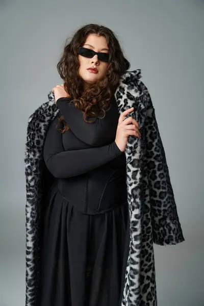 Confiante jeune femme courbée dans les lunettes de soleil se câlinant avec manteau de fourrure de léopard sur fond gris — Photo de stock