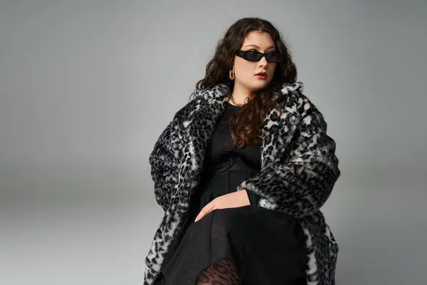 Ragazza curvy in pelliccia di leopardo e occhiali da sole seduto sulla sedia con gambe incrociate e cercando di lato — Foto stock