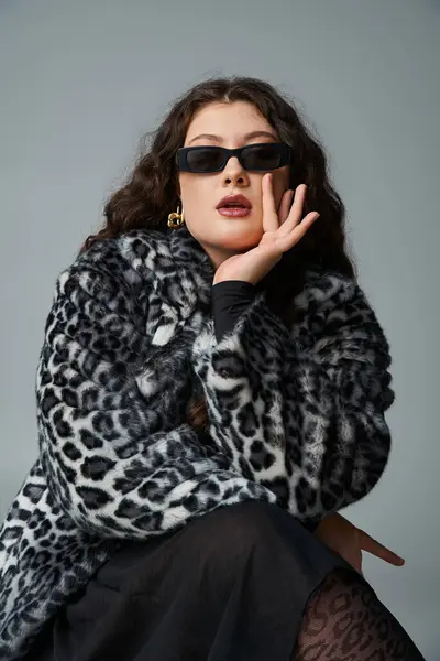 Bella donna curvy in pelliccia di leopardo e occhiali da sole seduti sulla sedia e mento a riposo a portata di mano — Foto stock