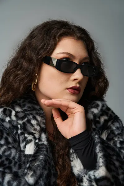 Portrait of glamourous curvy woman in sunglasses looking to side with chin on hand on grey — Stock Photo