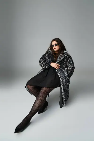 Розслаблений впевнений плюс розмір жінки в пальто і сонцезахисні окуляри, сидячи на чорному стільці — стокове фото