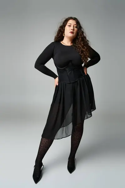 Charming plus size young woman putting leg to side with hands on waist on grey background — Stock Photo