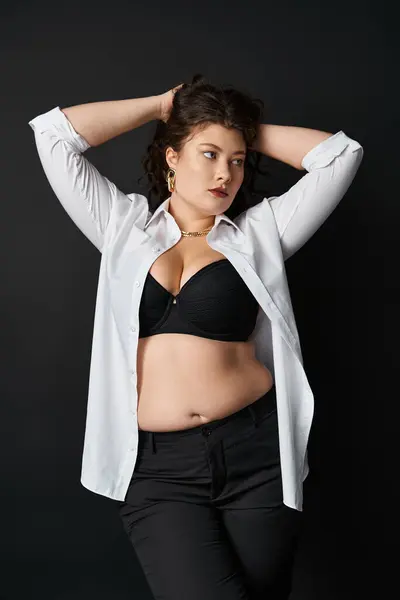 Lovely curvy woman in white shirt, black bra and pants putting hands behind head and holding hair — Stock Photo