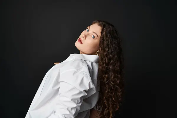 Pretty curvy woman in her 20s looking to camera from sideways against black background — Stock Photo