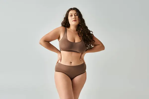 Beautiful curvy young woman in brown lingerie with curly hair posing hands on waist — Stock Photo