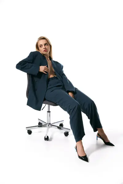 Привлекательная женщина с светлыми волосами в модном расстегнутом пиджаке сидит на стуле и смотрит в сторону — стоковое фото