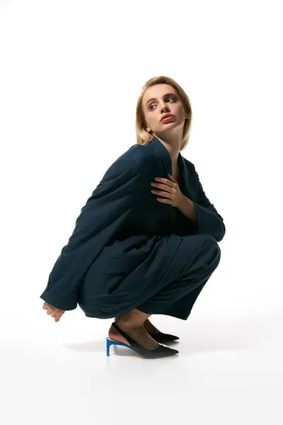 Atraente mulher graciosa com cabelo loiro em blazer azul sentado e olhando para longe no fundo branco — Fotografia de Stock