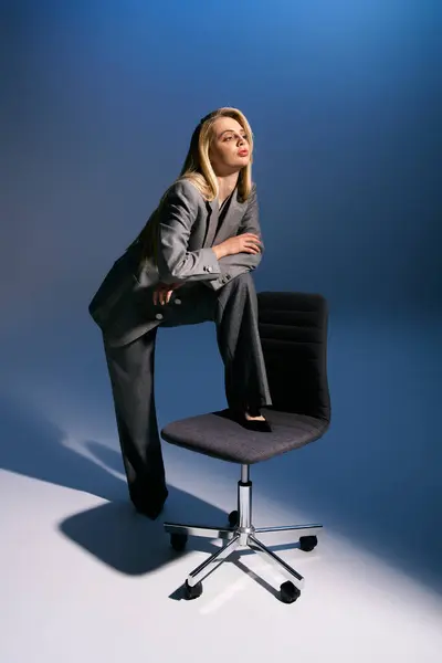 Соблазнительная элегантная женщина с светлыми волосами в смарт-серебристом костюме сидит на стуле и смотрит в сторону — стоковое фото