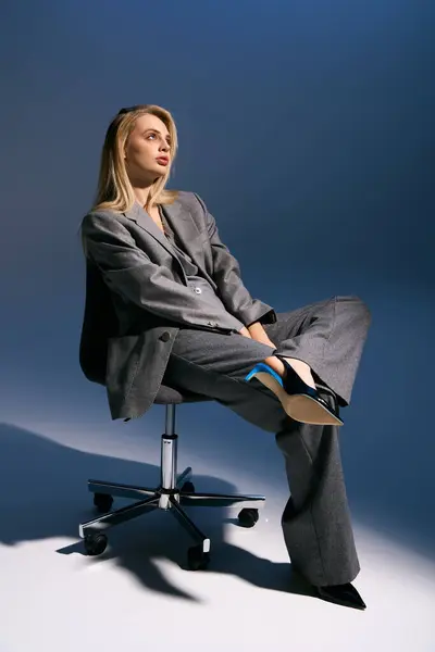 Atractiva joven en elegante esmoquin plateado con cabello rubio sentado en la silla y mirando hacia otro lado - foto de stock