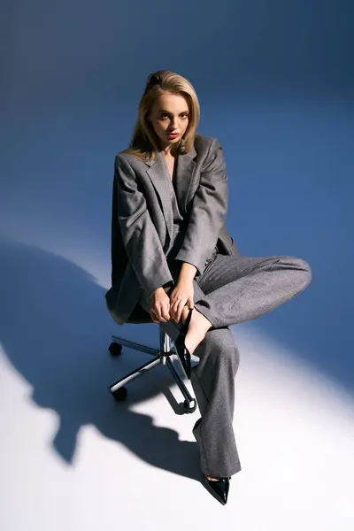 Attraente giovane donna in elegante smoking argento con capelli biondi seduti sulla sedia e guardando altrove — Foto stock