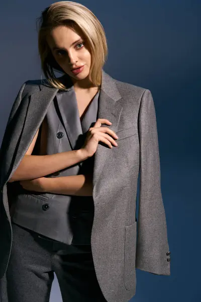 Elegant woman in silver chic vest and suit posing on dark blue backdrop and looking at camera — Stock Photo