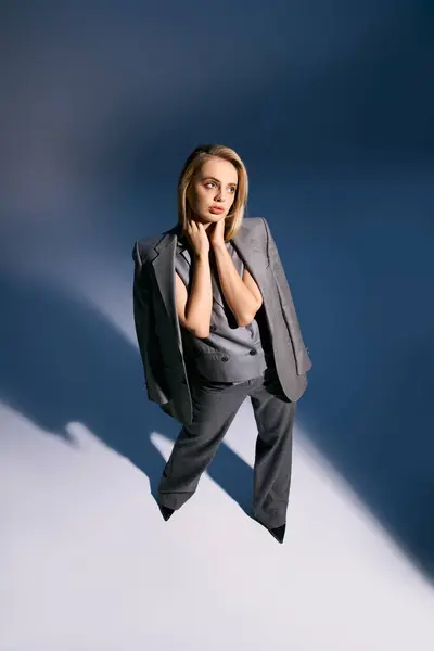 Attractive elegant woman with blonde hair in debonair vest and suit looking away on blue backdrop — Stock Photo