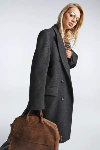 Красивая модная женщина в очках и коричневой сумке в черном элегантном пальто, смотрящая в камеру — стоковое фото