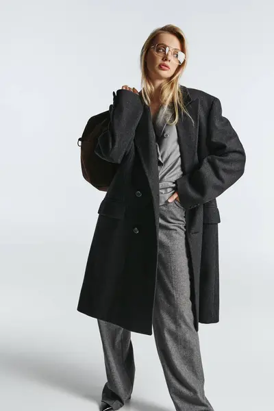 Atraente mulher graciosa com cabelo loiro em casaco elegante preto segurando saco marrom e olhando para longe — Fotografia de Stock