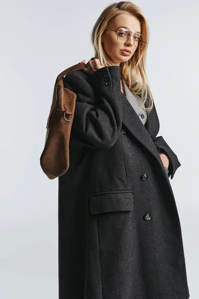 Bella donna alla moda con occhiali e borsa marrone in nero elegante cappotto guardando la fotocamera — Foto stock