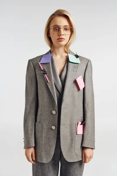 Zierliche Frau mit Brille im grauen schicken Anzug mit Büroklammern und Stift darauf und Blick in die Kamera — Stockfoto