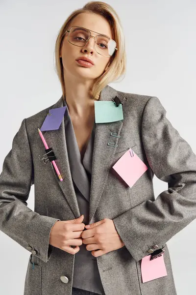 Zierliche Frau mit Brille im grauen schicken Anzug mit Büroklammern und Stift darauf und Blick in die Kamera — Stockfoto