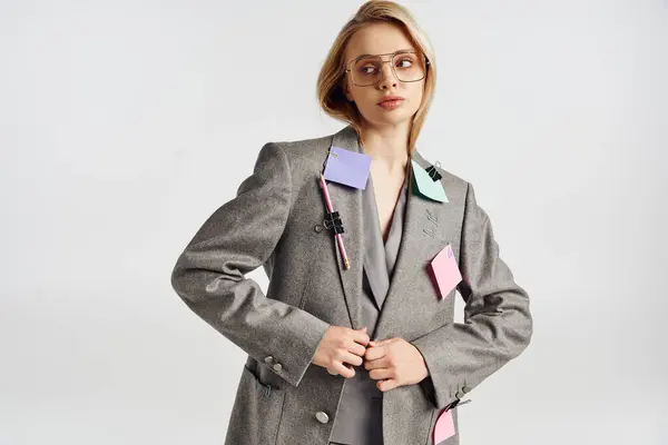 Attraktive junge Frau mit Brille im eleganten grauen Anzug mit Papeterie darauf und wegschauendem Blick — Stockfoto