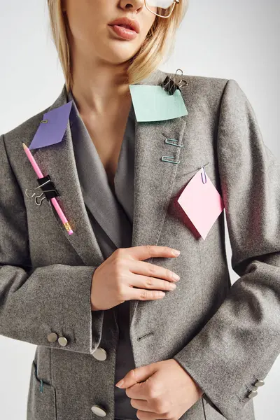 Vista cortada de jovem mulher elegante vestindo terno elegante com artigos de papelaria sobre ele em pano de fundo cinza — Fotografia de Stock
