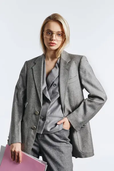 Schöne Frau mit stylischer Brille im grauen schicken Anzug posiert mit Papieren und blickt in die Kamera — Stockfoto