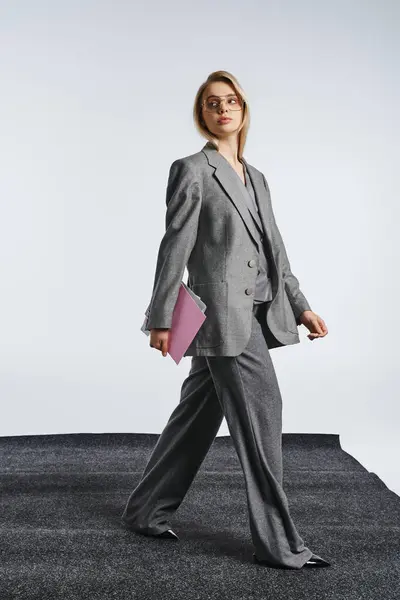 Schicke Frau mit stylischer Brille im grauen Anzug posiert mit Papieren und schaut weg — Stockfoto