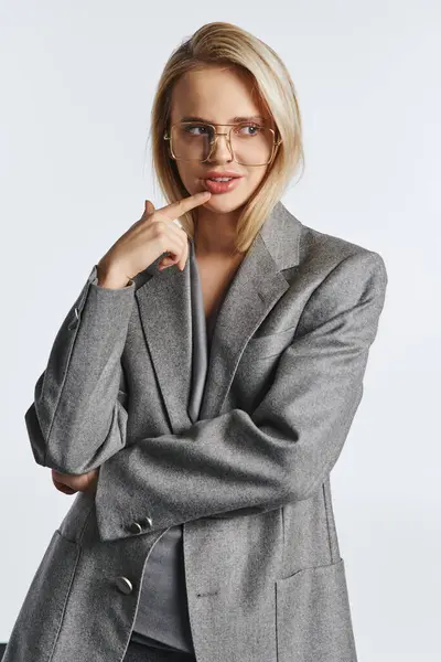 Mulher atraente alegre com óculos em terno elegante cinza posando no fundo cinza e olhando para longe — Fotografia de Stock