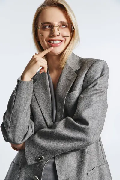 Cheerful attractive woman with glasses in gray stylish suit posing on gray backdrop and looking away — Stock Photo