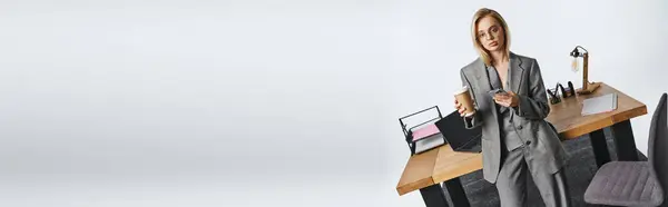Femme d'affaires sophistiquée en costume gris tenant smartphone et café et regardant la caméra, bannière — Photo de stock