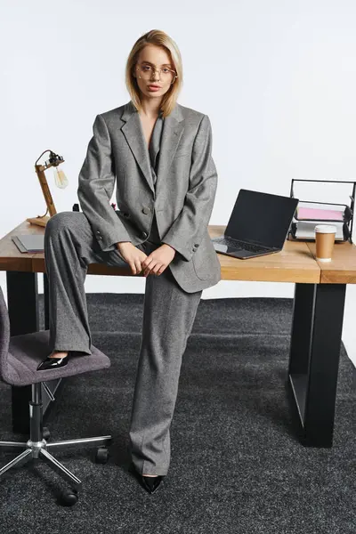 Красивая элегантная деловая женщина в сером нарядном костюме позирует рядом со столом и смотрит в камеру — стоковое фото