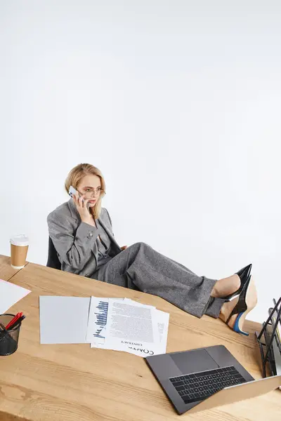 Elegante Geschäftsfrau im schicken grauen Anzug mit stylischer Brille telefoniert am Schreibtisch — Stockfoto