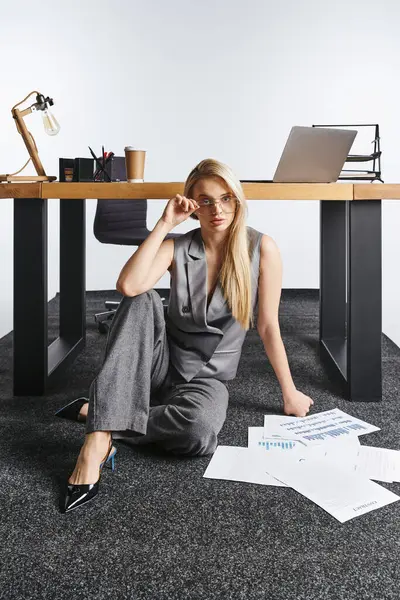 Blonde Frau im eleganten grauen Anzug, die mit ihren Papieren auf dem Boden arbeitet und in die Kamera blickt — Stockfoto