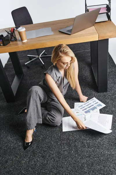 Atractiva mujer de moda en traje inteligente trabajando en el suelo con papeleo y mirando hacia otro lado - foto de stock