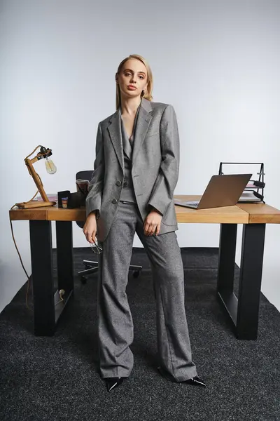 Attractive hard working businesswoman in sophisticated gray suit looking at camera on gray backdrop — Stock Photo