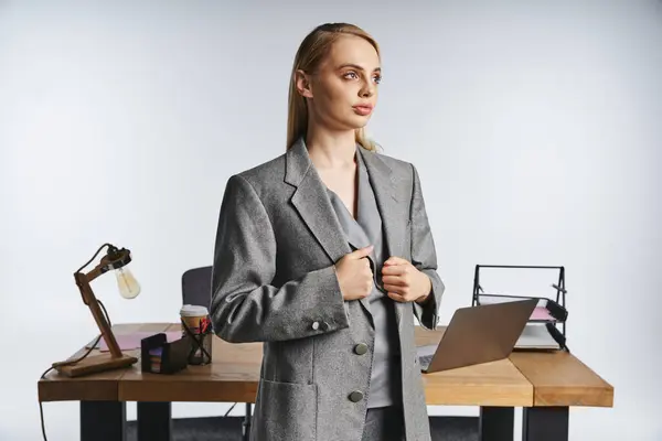 Debonair gut aussehende Geschäftsfrau im eleganten grauen Anzug mit blonden Haaren schaut weg — Stockfoto