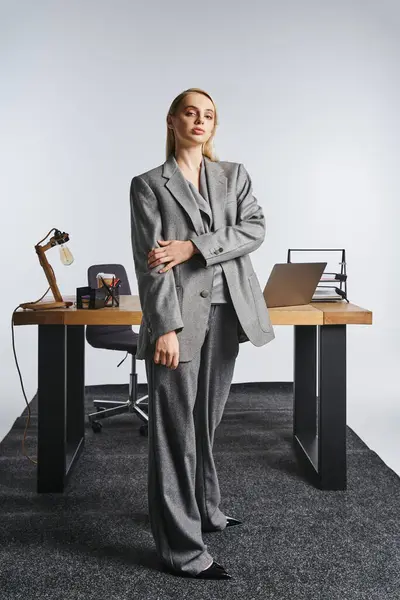 Attractive hard working businesswoman in sophisticated gray suit looking at camera on gray backdrop — Stock Photo