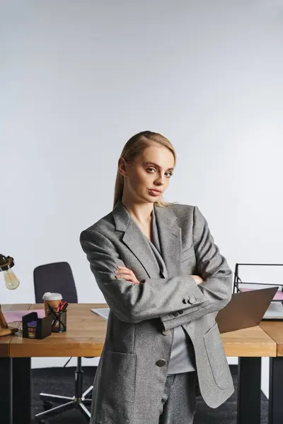 Atractiva mujer de negocios trabajadora en traje gris sofisticado mirando a la cámara en el fondo gris - foto de stock