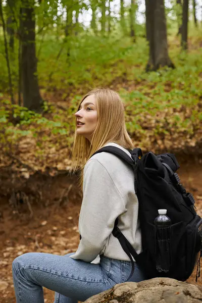Seitenansicht der gemütlich lächelnden blonden Wanderin, die sich auf Felsen ausruht, mit Blick auf den friedlichen Waldblick — Stockfoto
