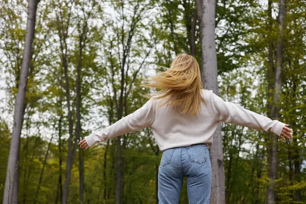 Back view of blonde woman explorer dancing in forest in scenic peaceful setting, freedom — Stock Photo