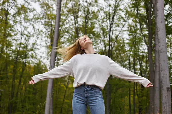 Peaceful and relaxed blonde woman dancing in forest jeans and sweater on backpacking trip — Stock Photo