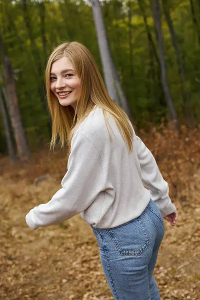 Joyeuse jeune femme randonneuse courant dans les bois d'automne et regardant la caméra avec le sourire — Photo de stock